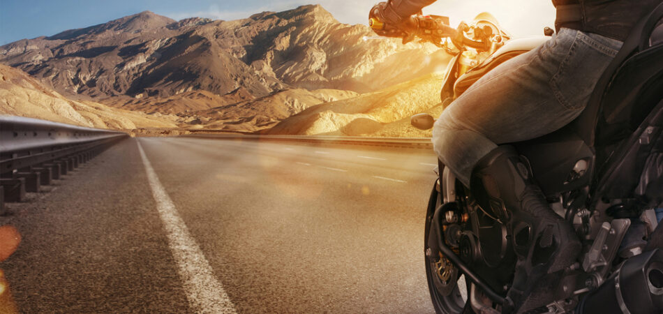 Biker,riding,motorcycle,on,an,empty,road,at,sunny,day